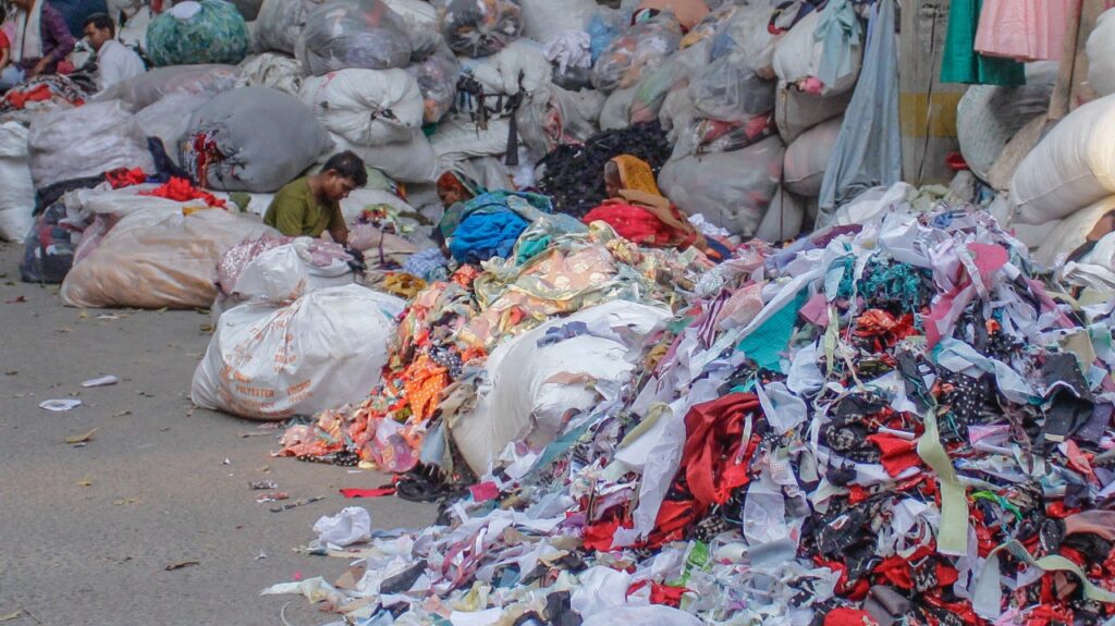 Heaps of textile waste and fabric scraps being sorted by workers in a garment recycling area, showing the scale of fashion industry waste and the importance of textile waste management.
